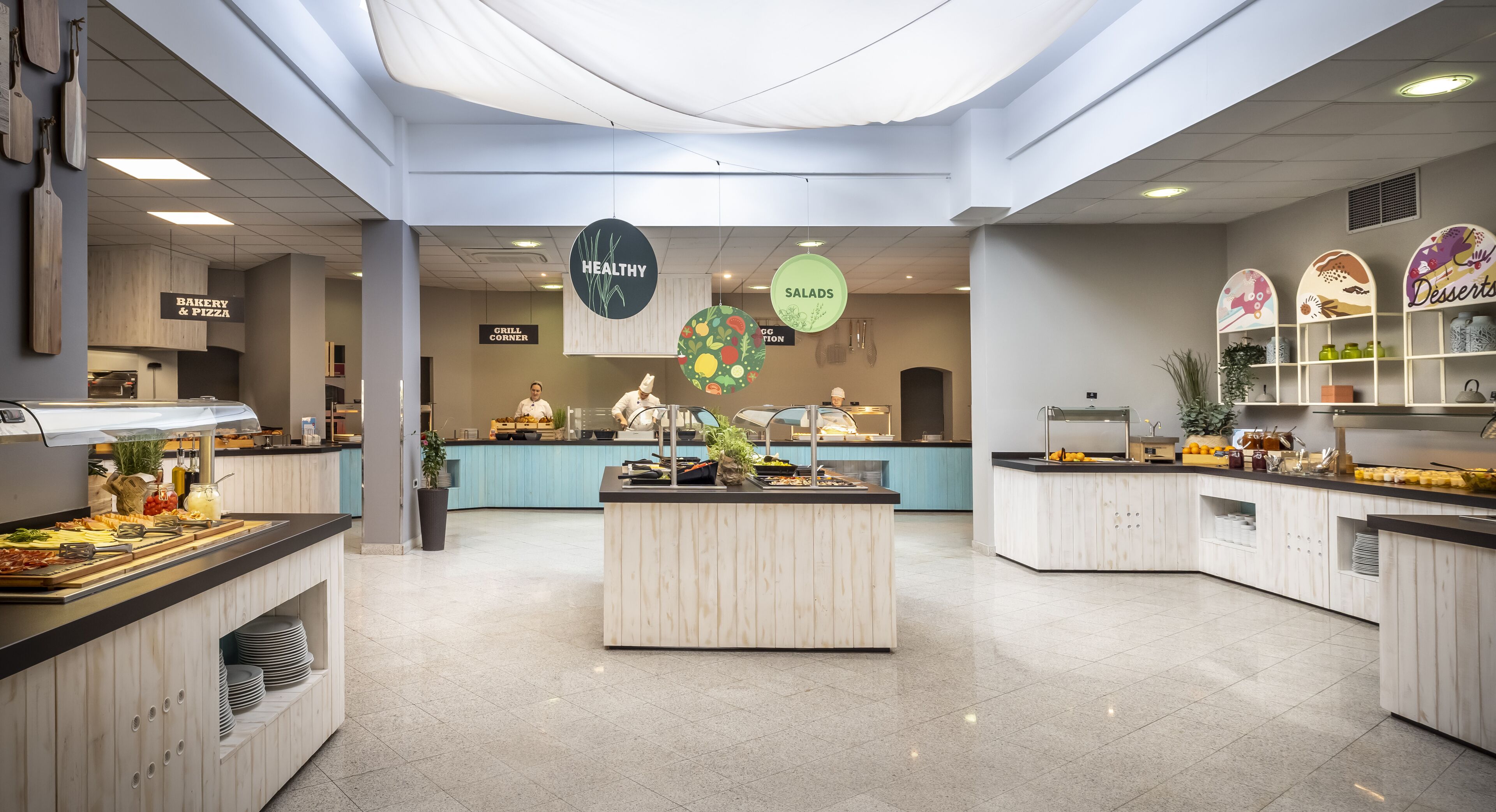 A modern cafeteria with a central island, various food stations, and clear signage for different food sections.