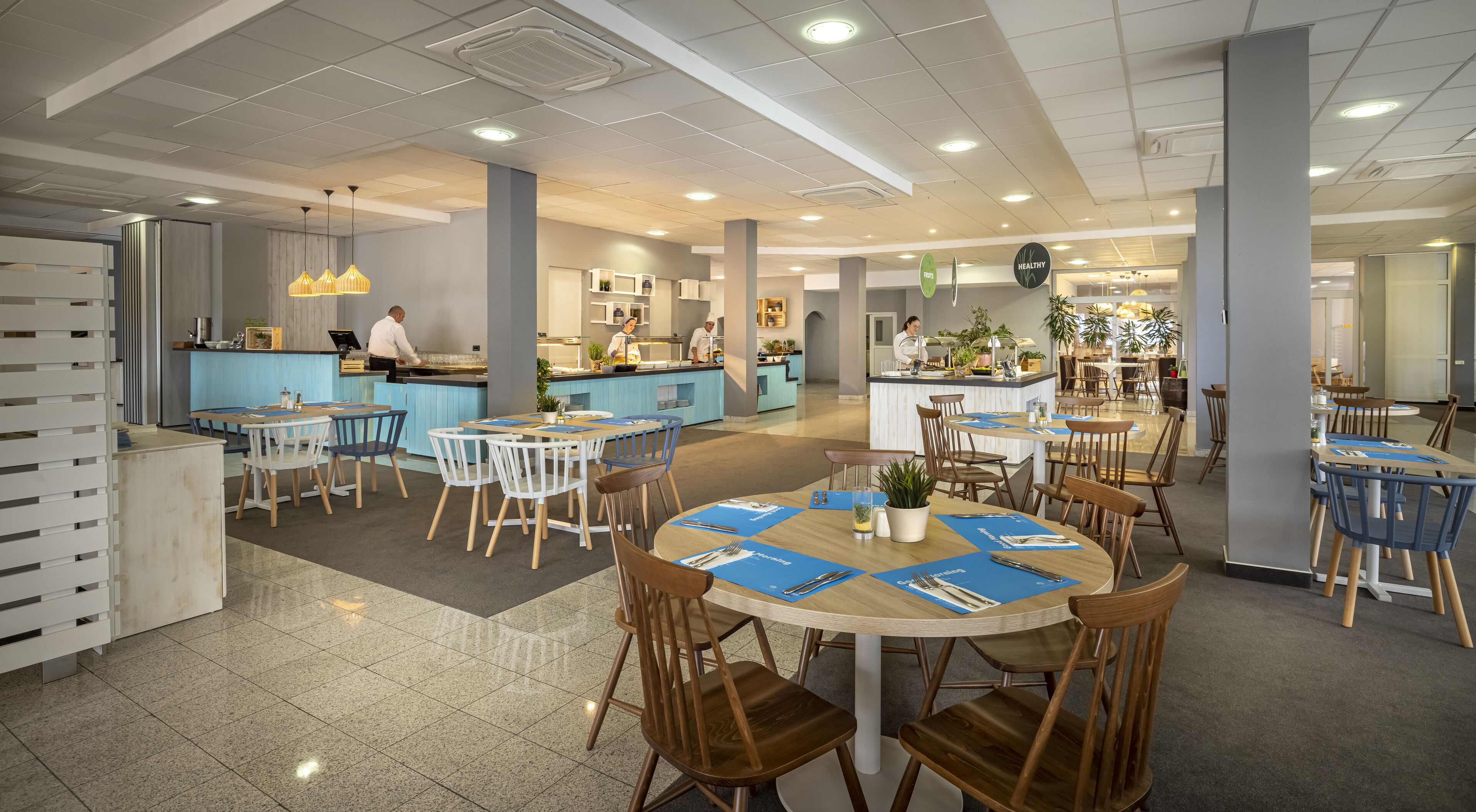 A modern restaurant with round tables, blue placemats, and wooden chairs.
