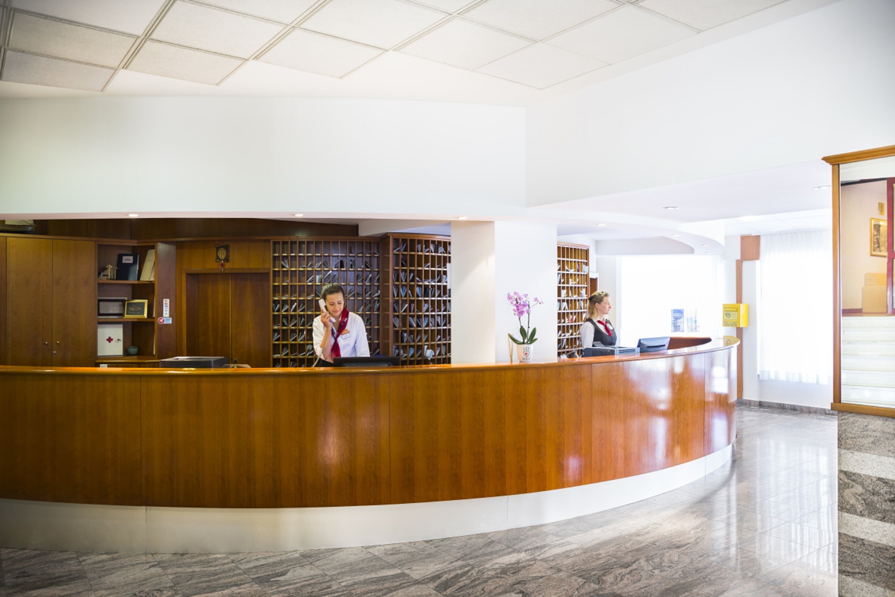 A reception desk with a wooden finish, a marble floor, and a large bookshelf filled with books.