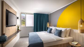A modern bedroom with a large bed, a TV mounted on the wall, a window with curtains, and a yellow accent wall.
