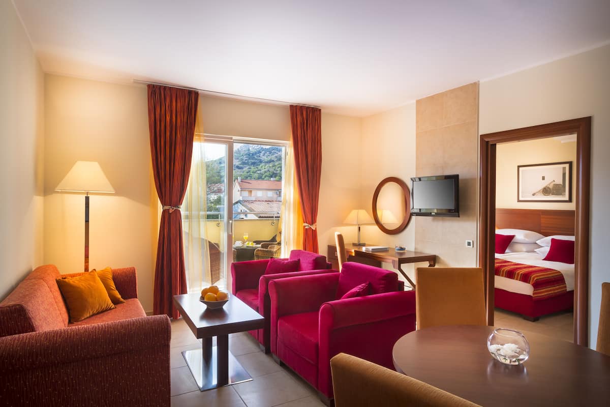 Habitación de hotel con sofá, sillón, mesa y cama con ropa de cama roja.