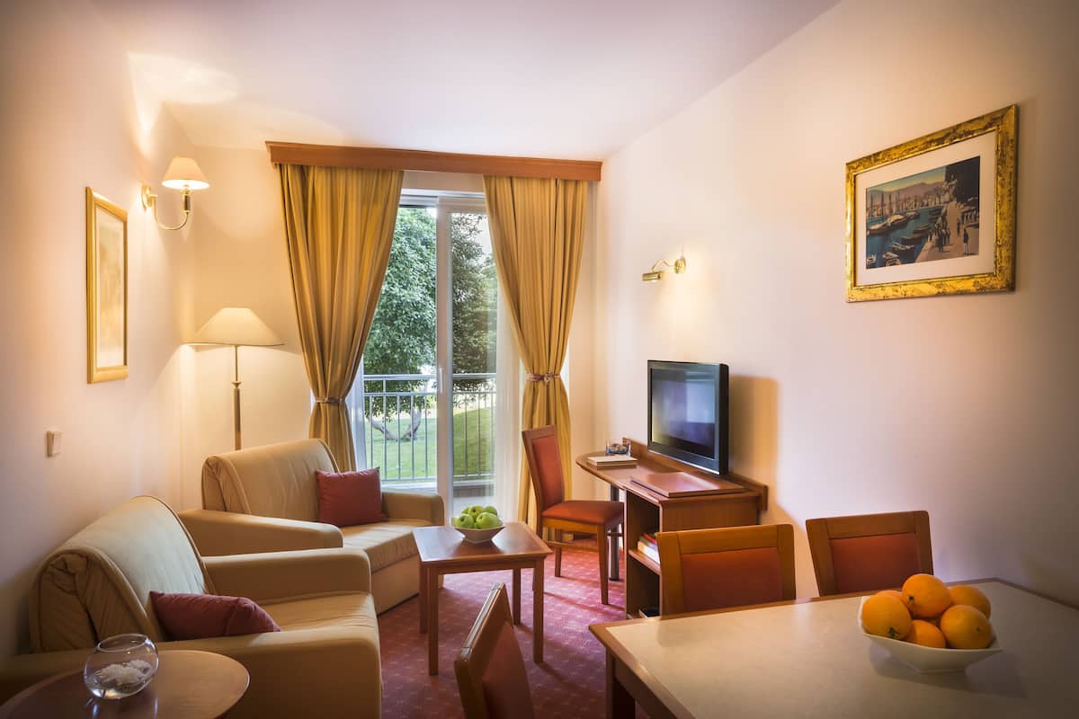 Habitación de hotel con sofá, sillón, mesa de comedor, televisión y un frutero.