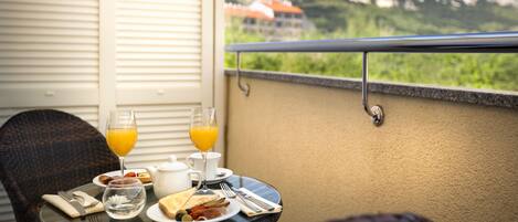 Un balcon avec une table dressée pour le petit-déjeuner, comprenant des toasts, des œufs et du jus d’orange, offrant une vue sur un paysage montagneux.