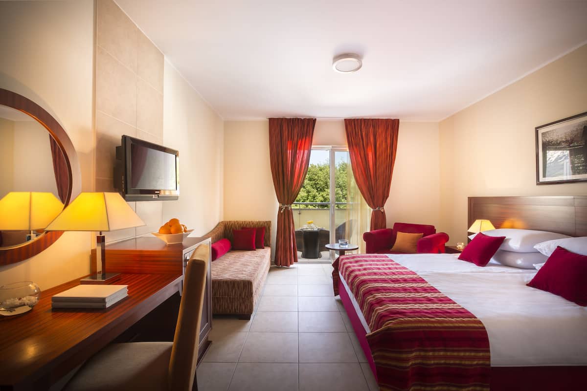 Habitación de hotel con cama, escritorio con lámpara, televisión, silla y una mesita con un bol de fruta.