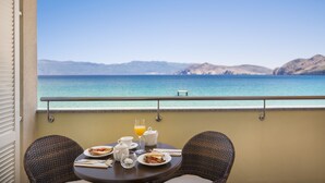A balcony with a table set for breakfast, overlooking a coastal view with mountains in the distance.