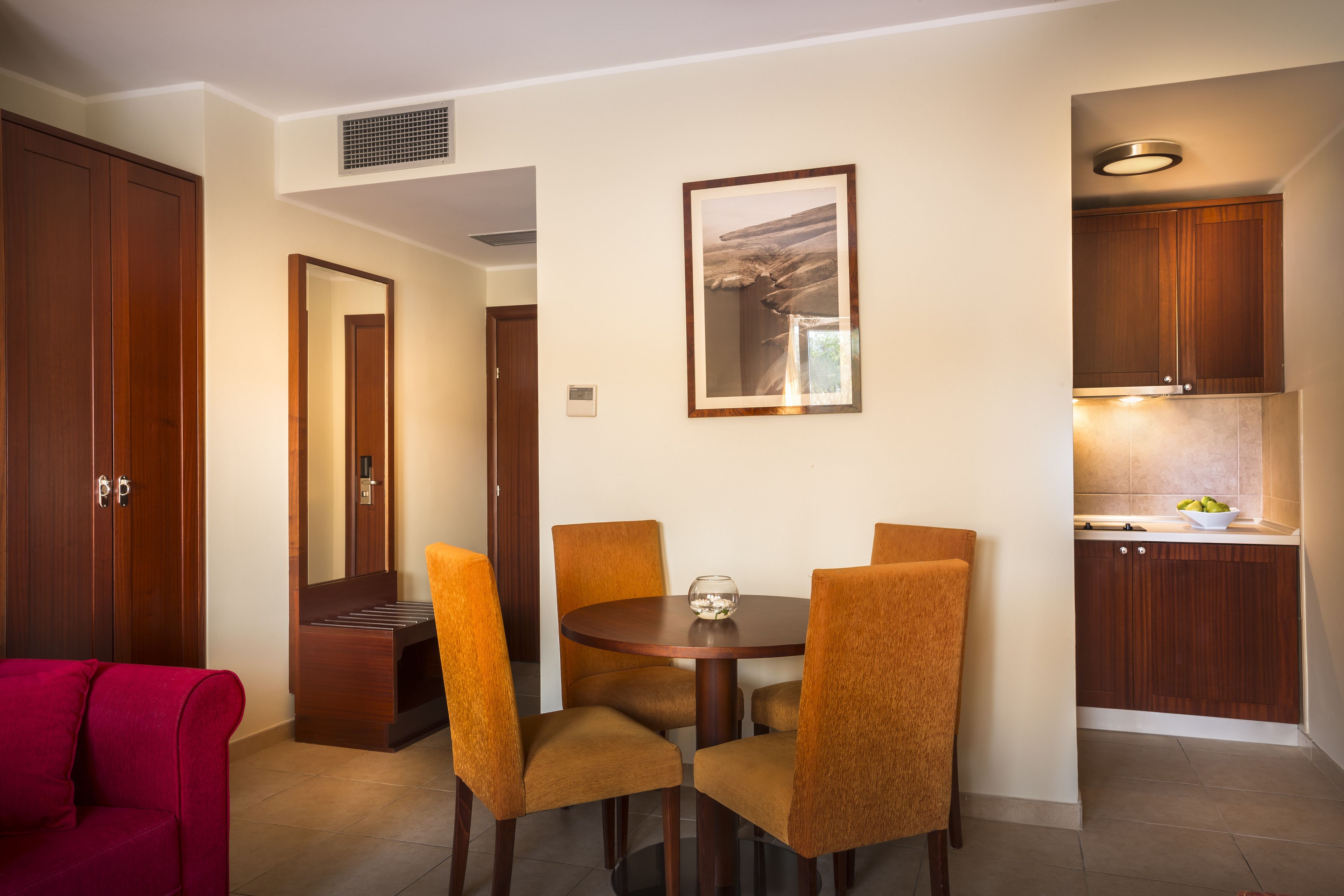 A dining area with a round table and four chairs, a red sofa, wooden cabinets, and a framed picture on the wall.