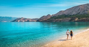 Une plage bordée d’une eau turquoise et limpide, avec des montagnes rocheuses en arrière-plan.