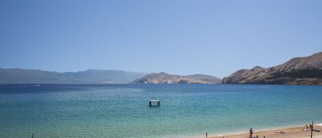 A beach with clear blue water, a small dock, and people relaxing on the sand.