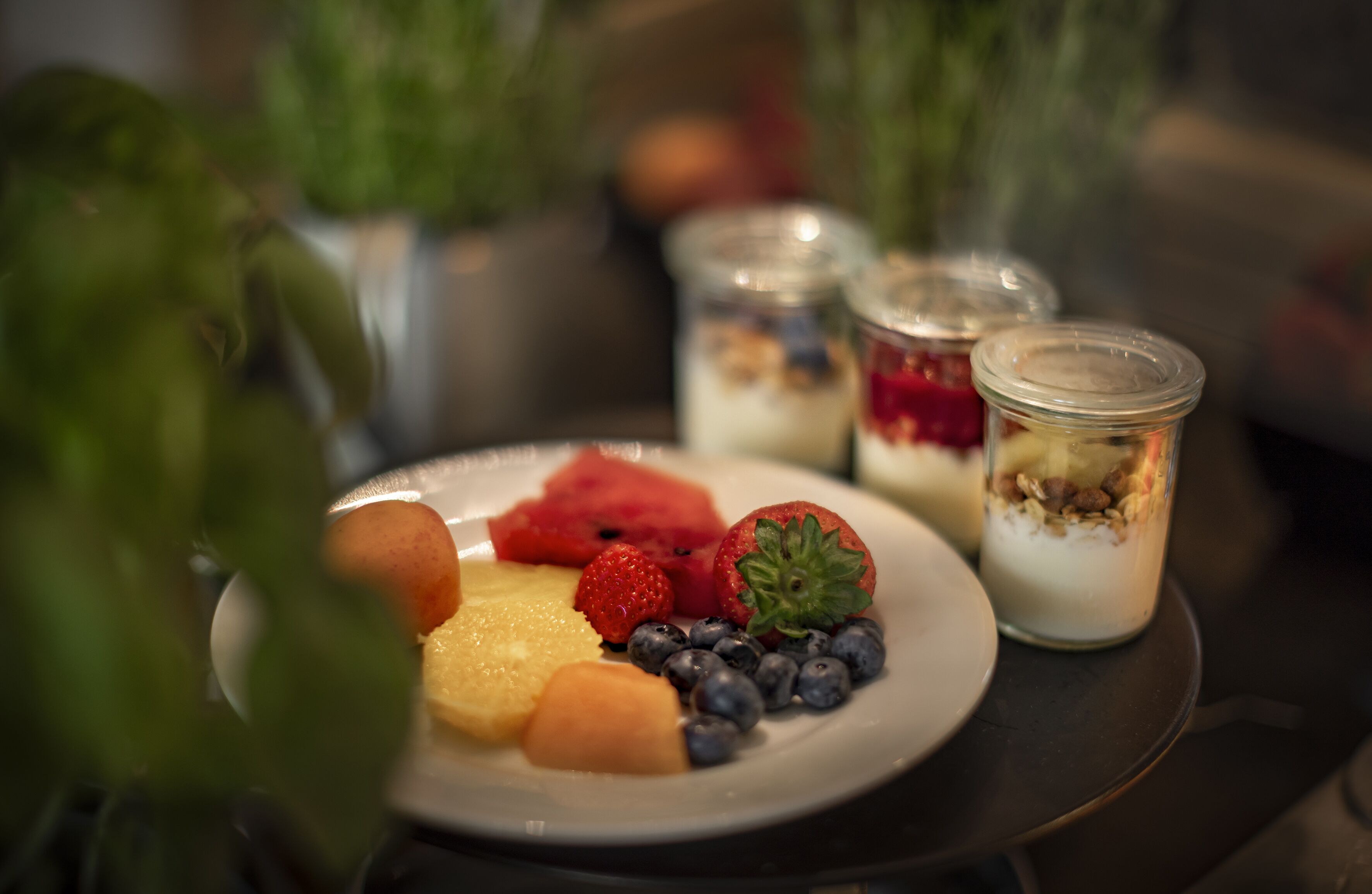 Un plato de fruta y vasos de parfait de yogur sobre una mesa.