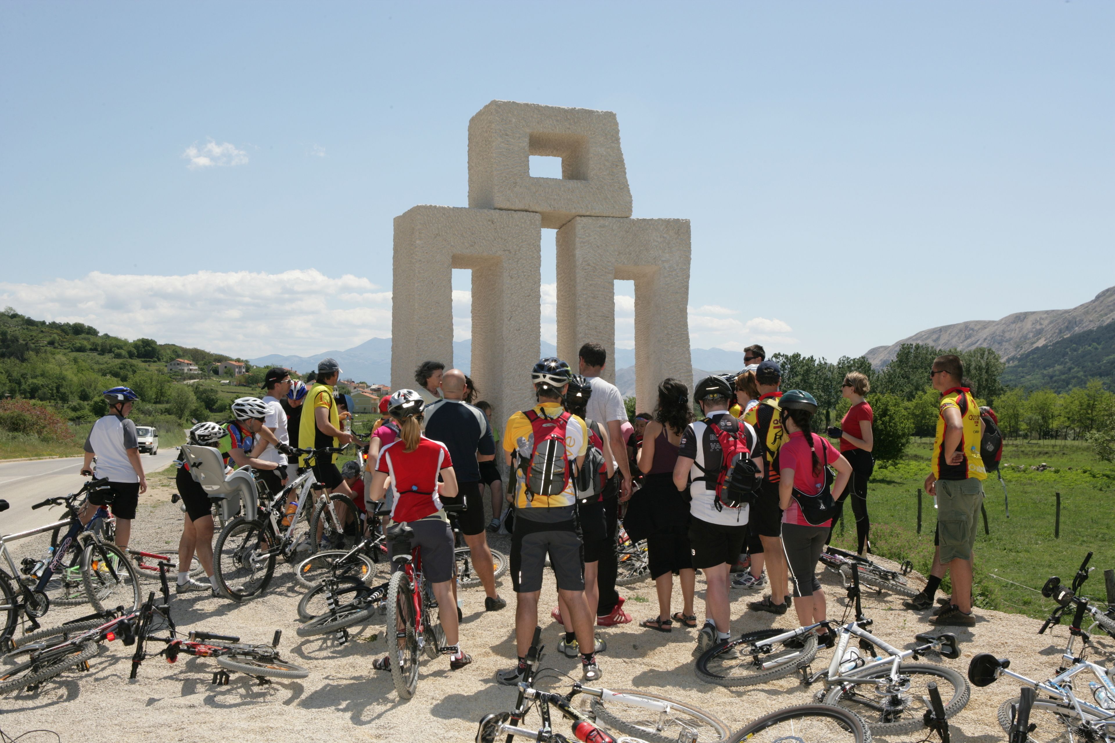 A group of cyclists gathered around a large stone monument in a rural setting.