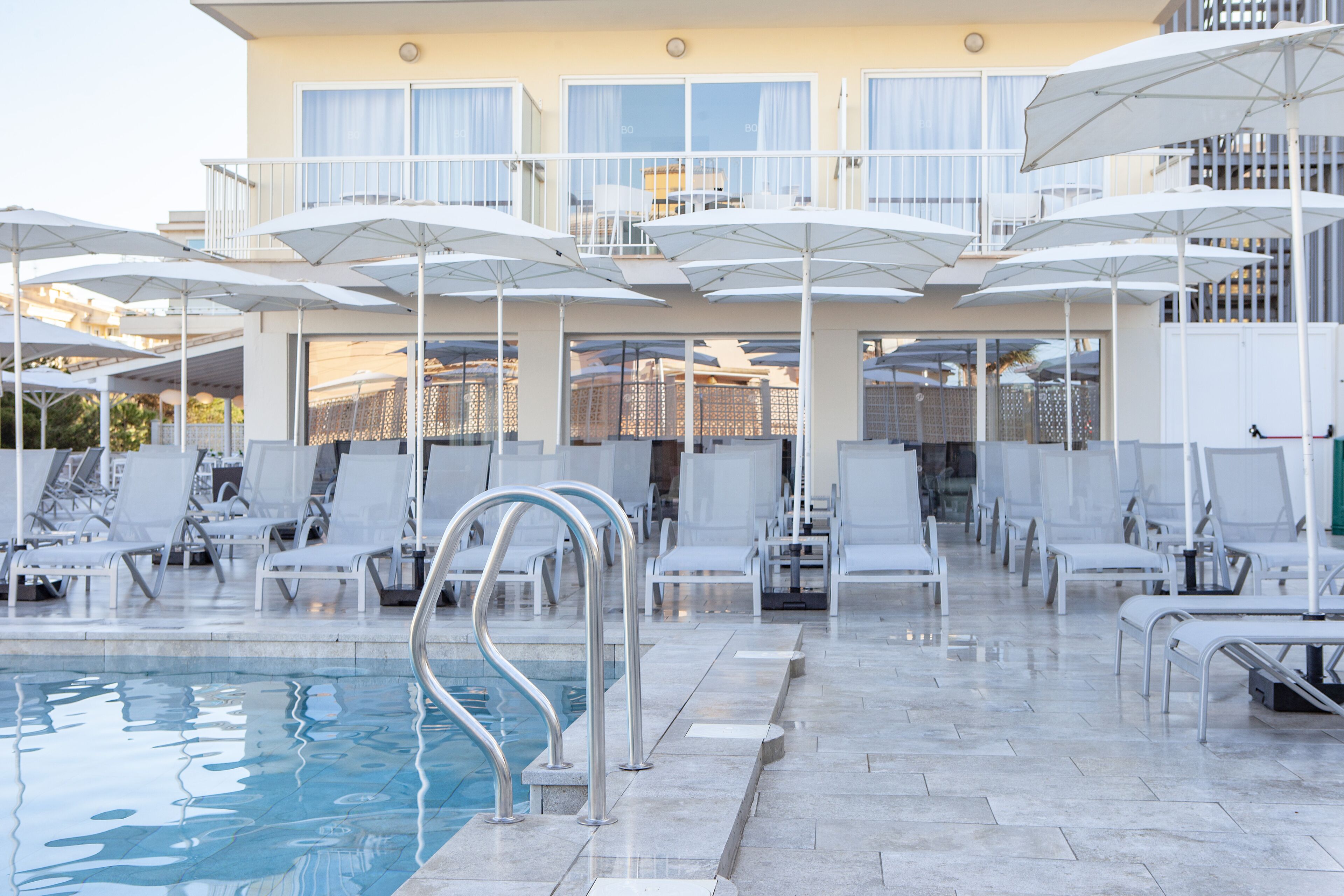 A pool area with multiple white umbrellas, lounge chairs, and a clear pool.