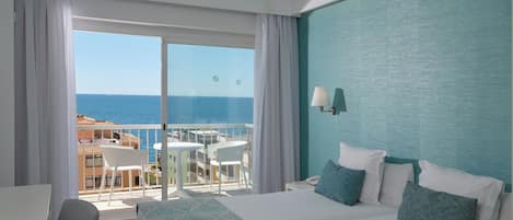A hotel room with a balcony, a bed, a desk, and a view of the sea.