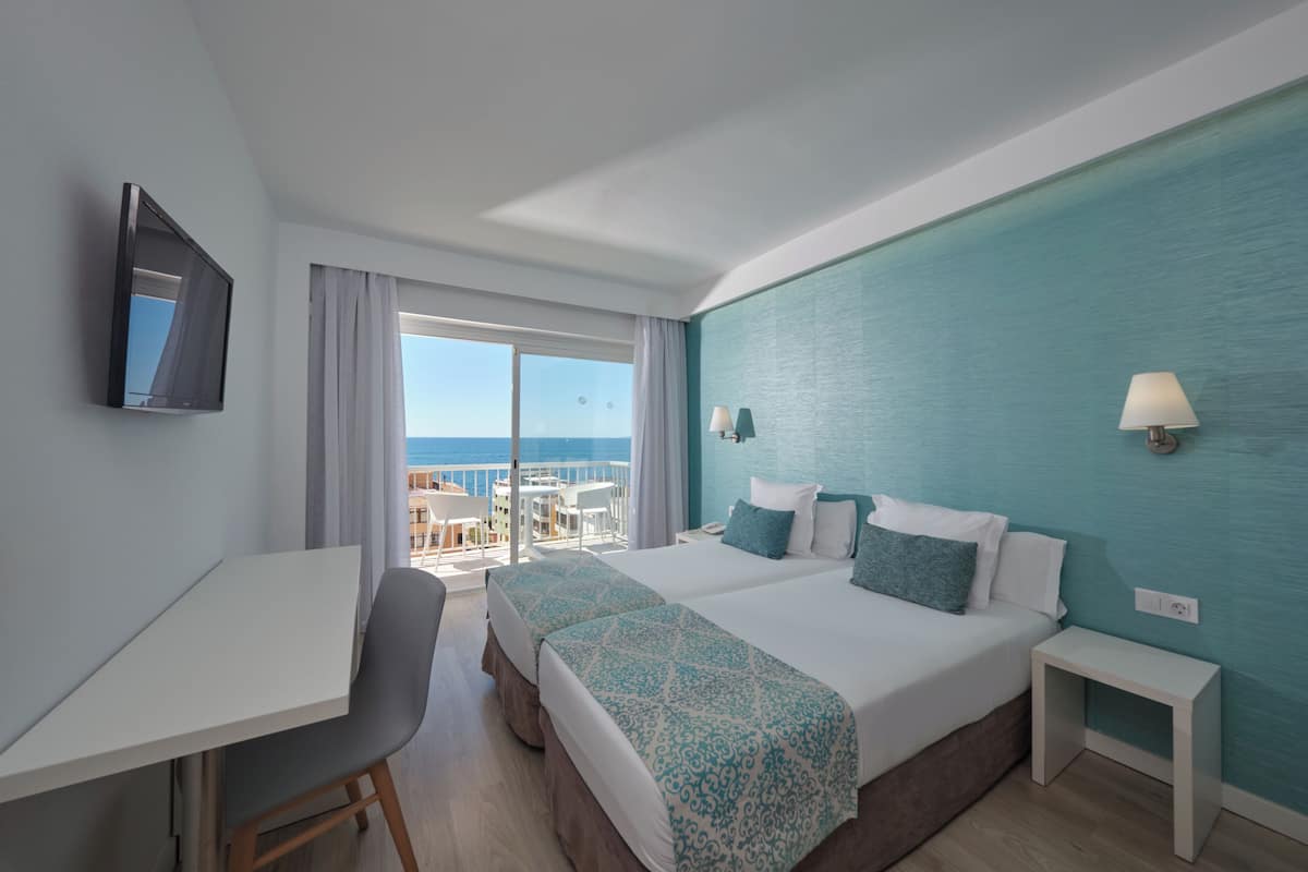 A hotel room with a balcony, two beds, a desk, and a TV.