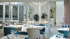 A restaurant with multiple tables and chairs, large windows, and indoor plants. - BQ Apolo Hotel (Palma de Mallorca)