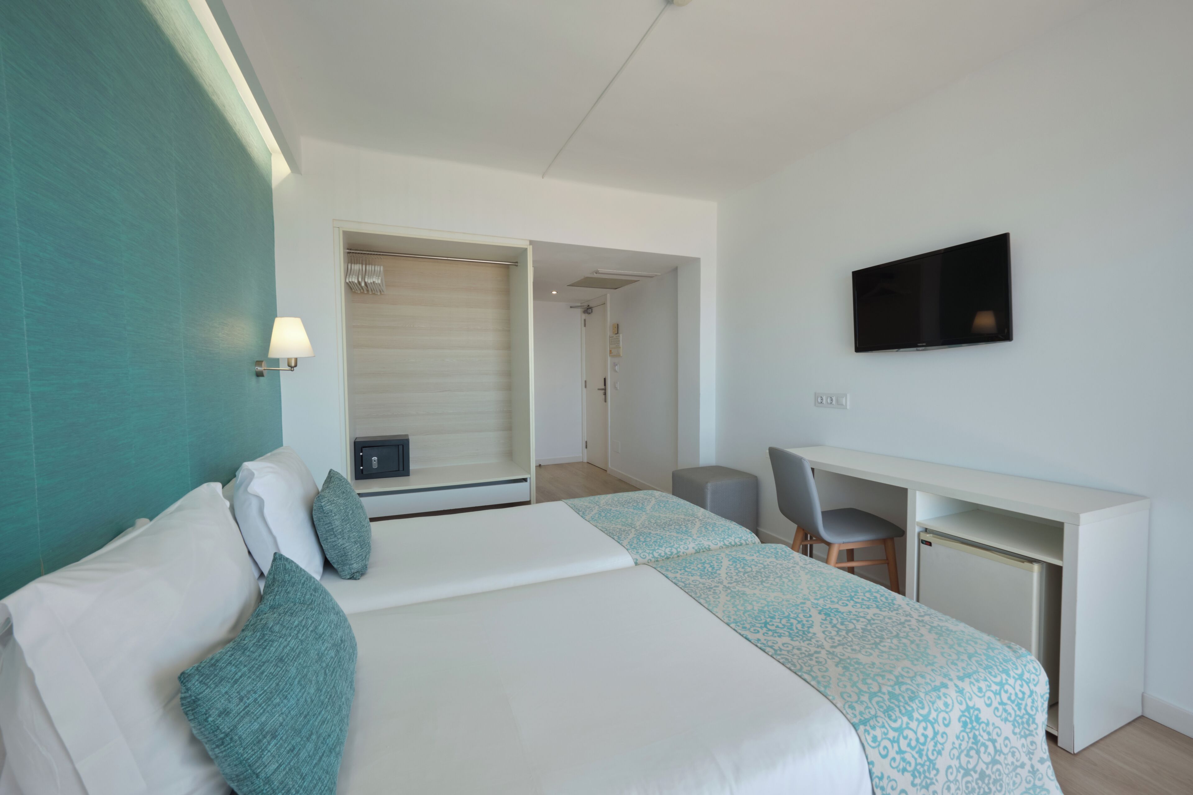 A hotel room with a bed, a desk, a chair, a television, and a door leading to another room.