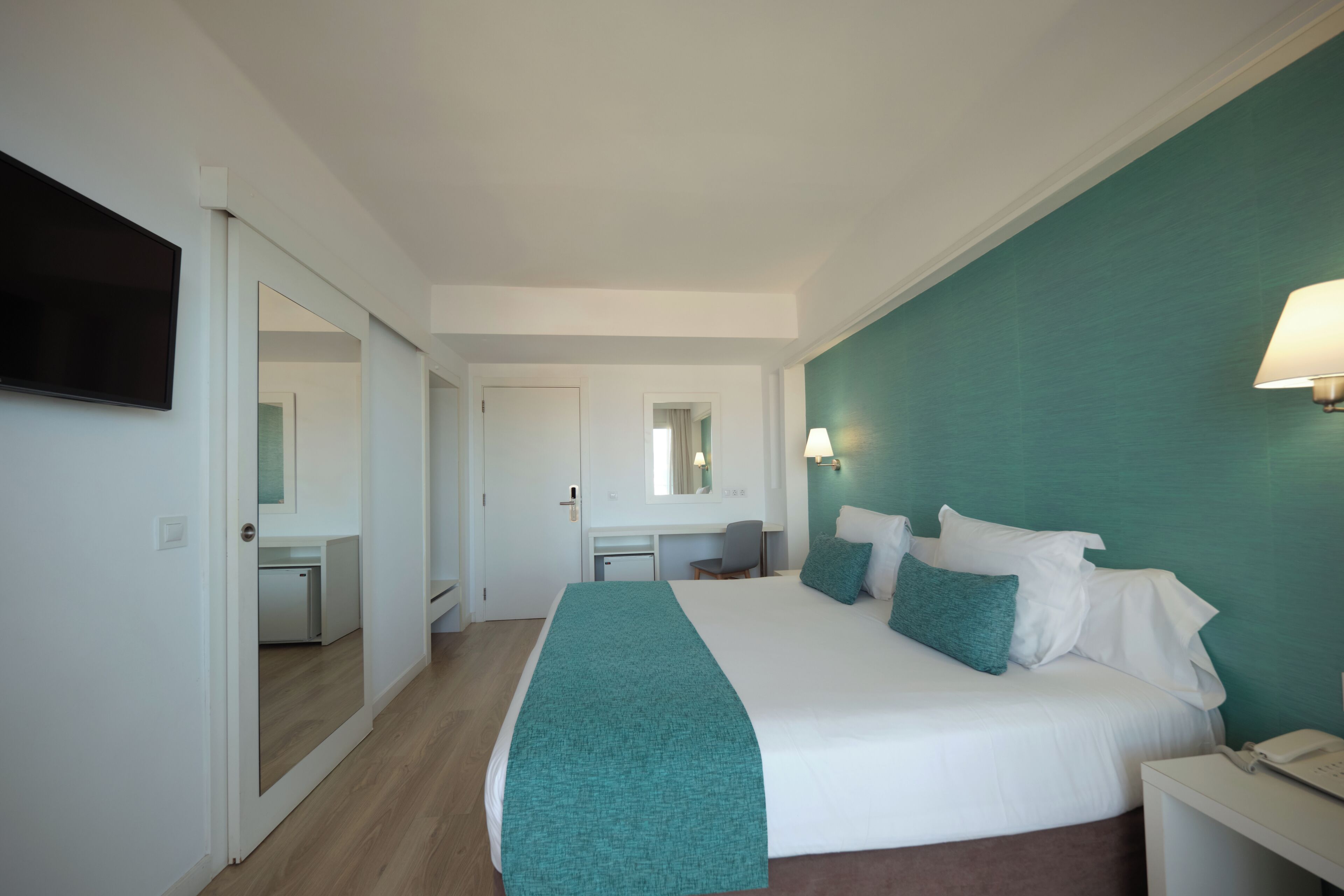 Habitación de hotel con cama, escritorio, silla, televisor y lámpara.