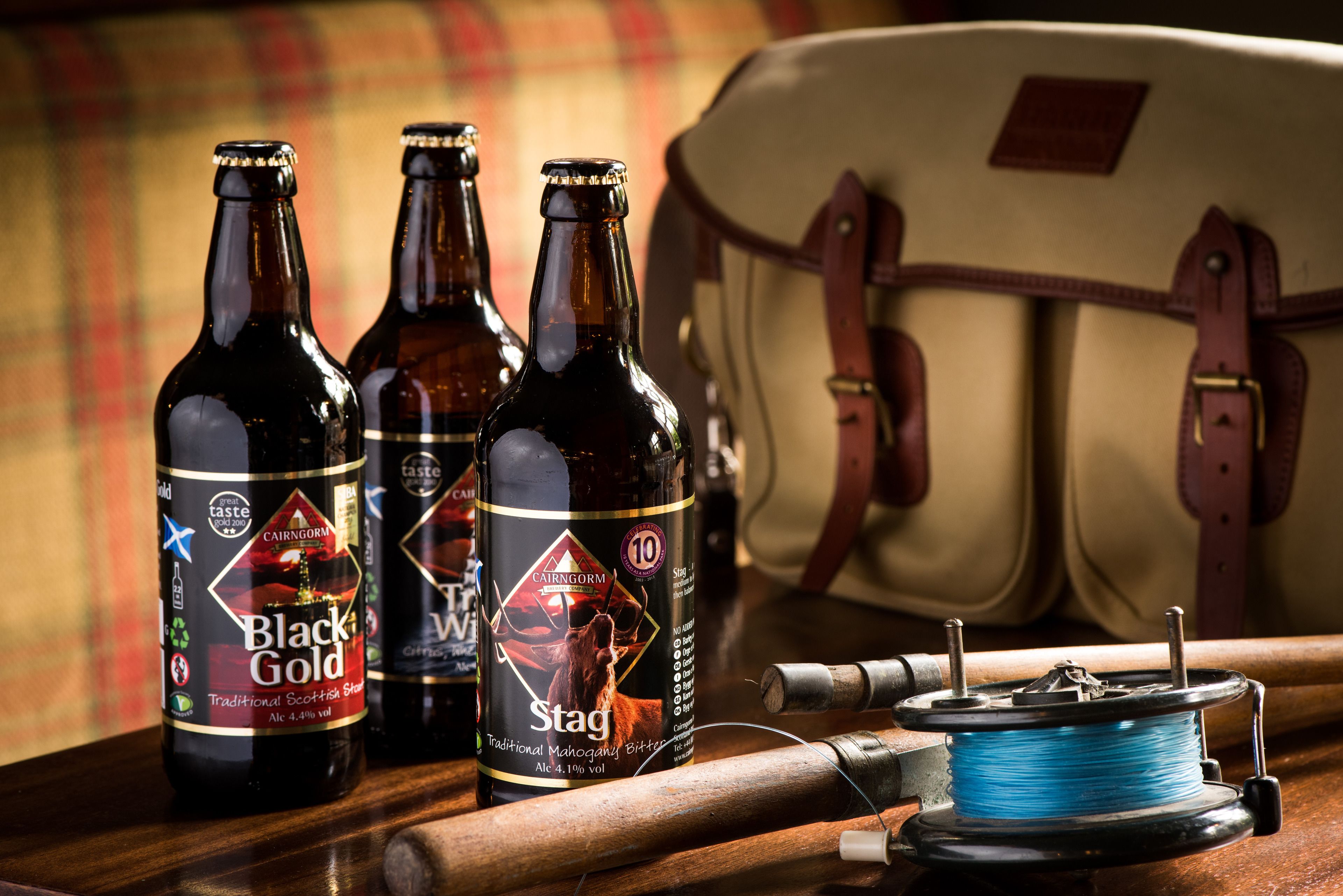 Three bottles of beer, a spool of blue thread, and a leather bag on a wooden surface.