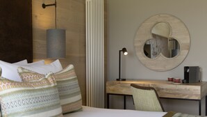 A hotel room with a bed, pillows, a desk, a chair, a lamp, a coffee maker, and a mirror.