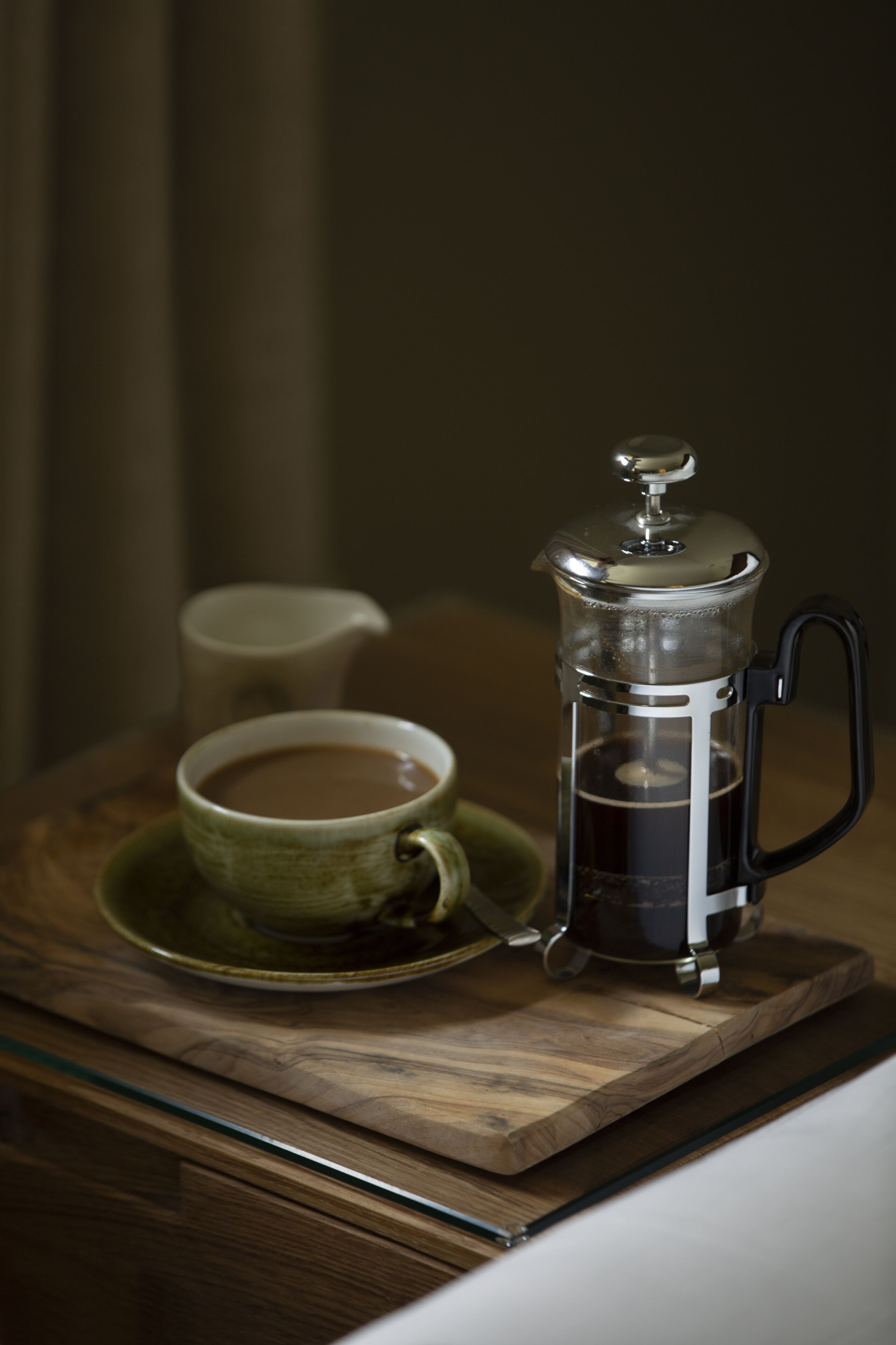 Uma cafeteira francesa em uma bandeja de madeira, com uma xícara de café e um bule.