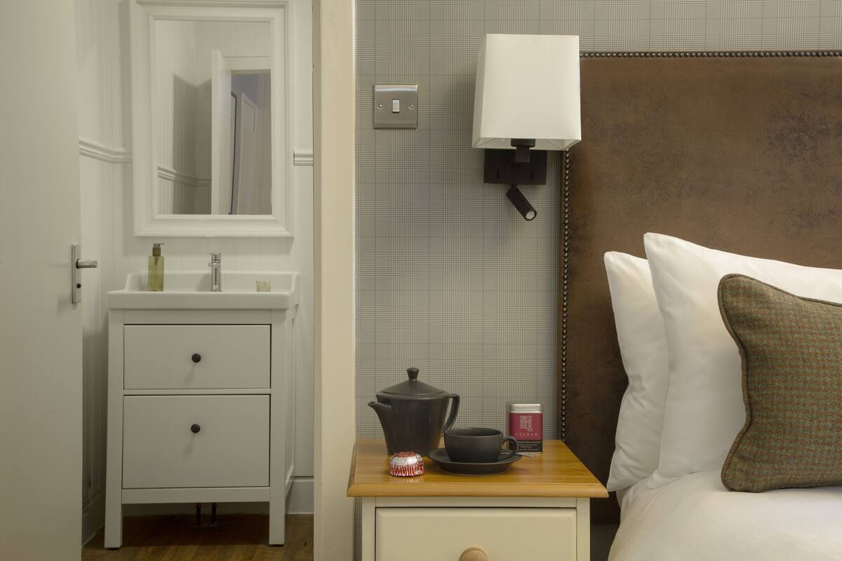 A neatly arranged bedroom with a bed, bedside table, lamp, and a small cabinet.