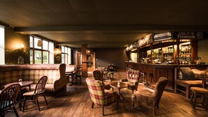A cozy bar area with wooden flooring, plush seating, and a bar stocked with bottles. - Balmoral Arms (Ballater)
