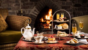 A cozy room with a brick fireplace, a three-tiered tea service, and a variety of snacks and drinks on a table. - Balmoral Arms (Ballater)