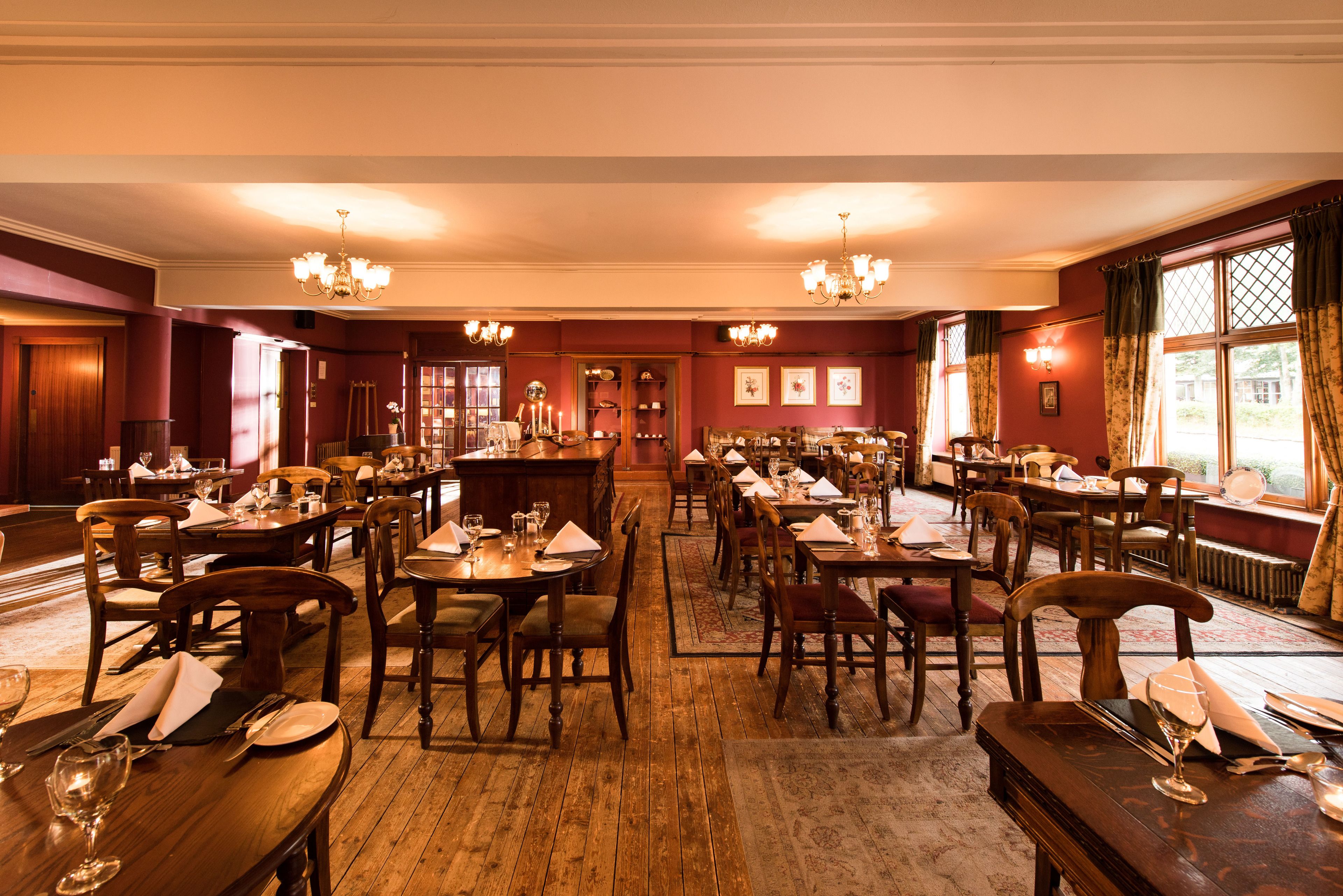 Une salle à manger élégante, avec des tables et des chaises en bois, des lustres et de grandes fenêtres ornées de rideaux.