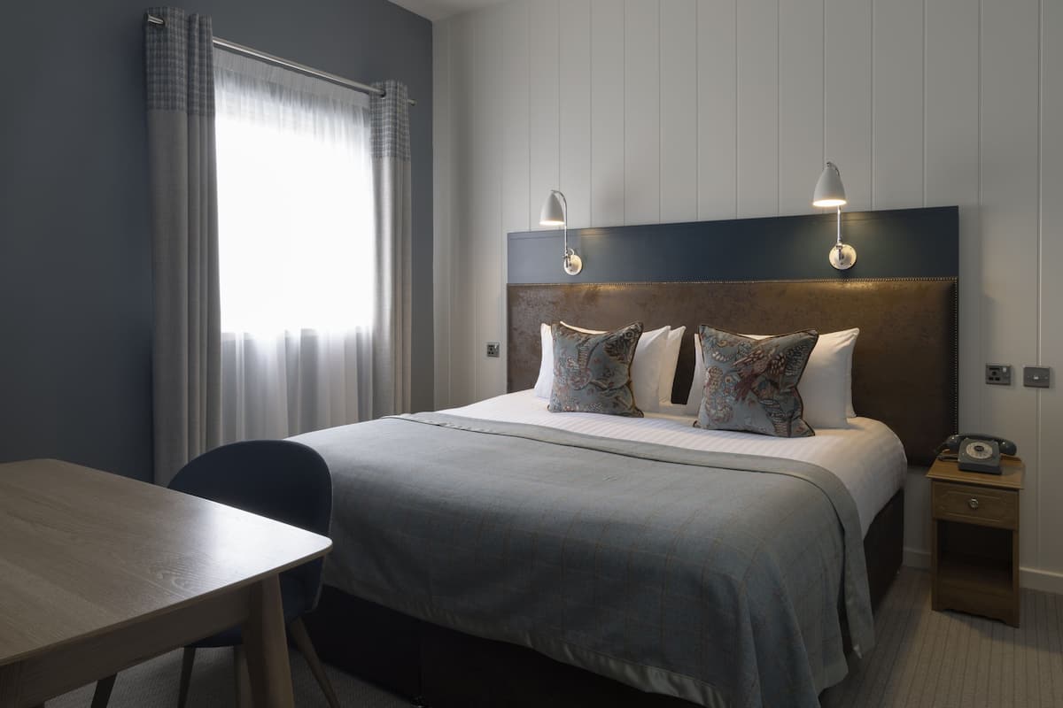 A hotel room with a large bed, two bedside lamps, a desk, and a chair.