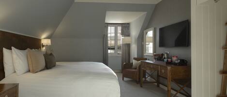 A bedroom with a large bed, a desk, a chair, a TV, and a window with curtains.