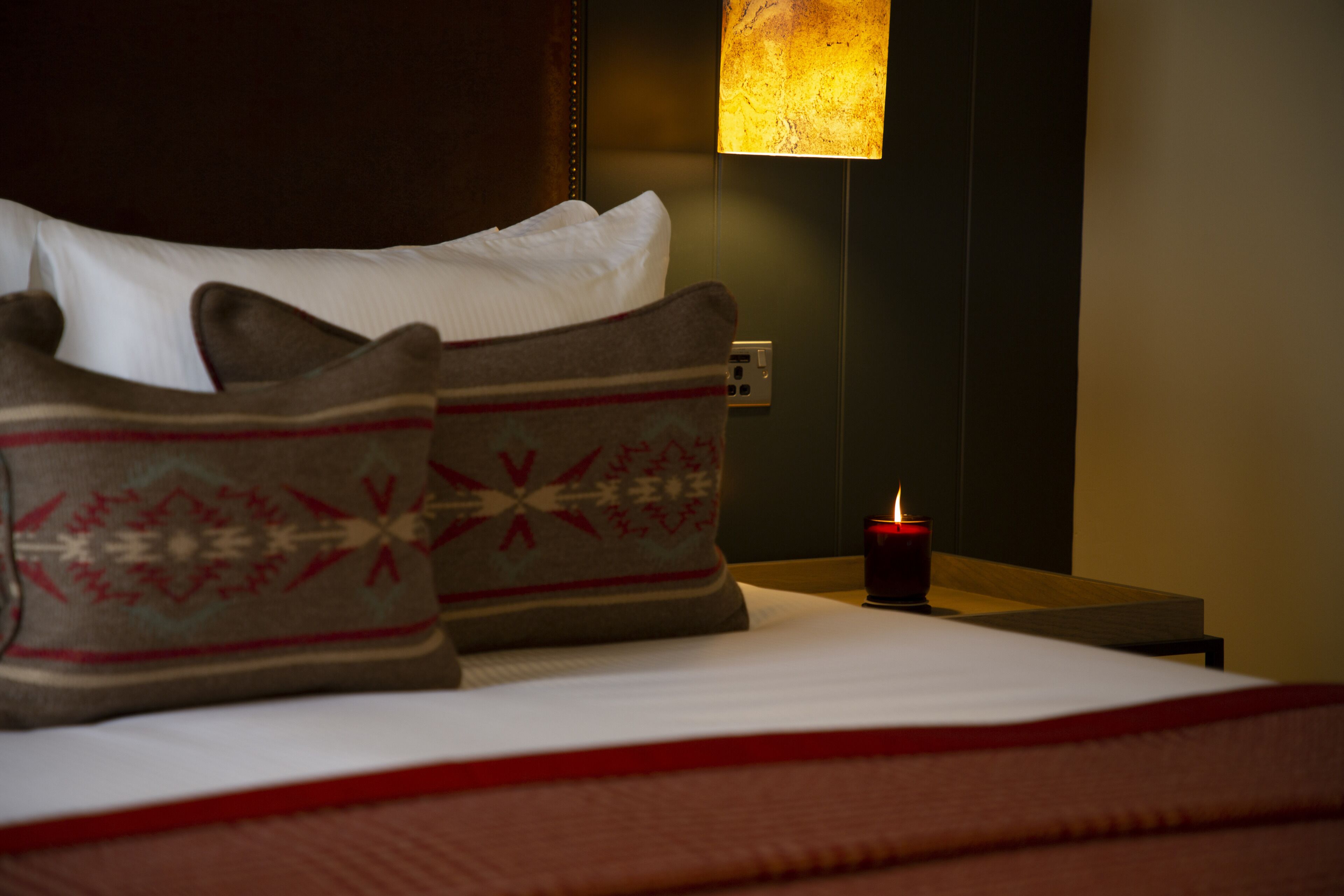 A neatly made bed with patterned pillows and a lit candle on a bedside table.