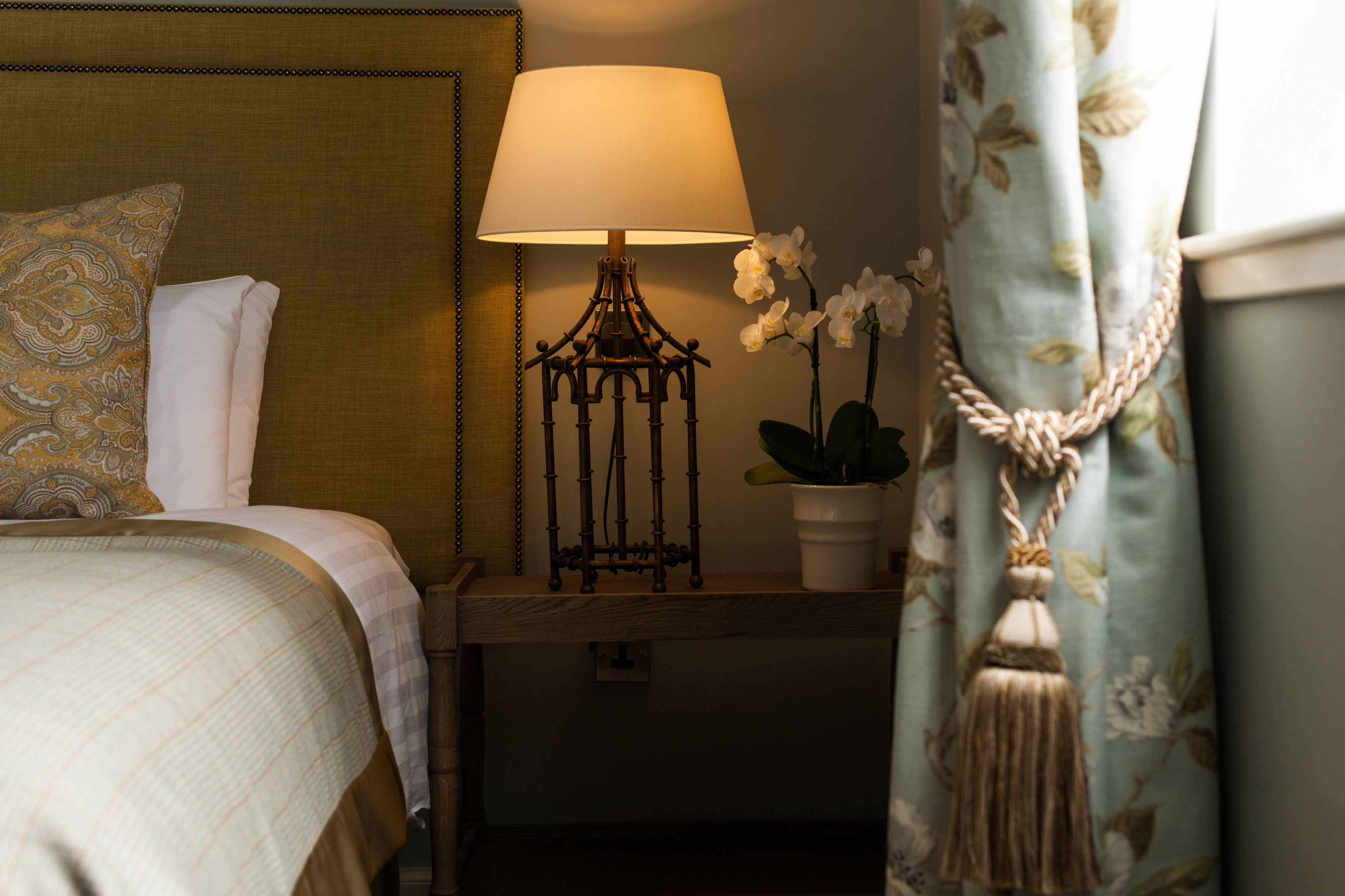 A neatly made bed with a patterned pillow, a bedside table with a lamp, and a potted orchid.