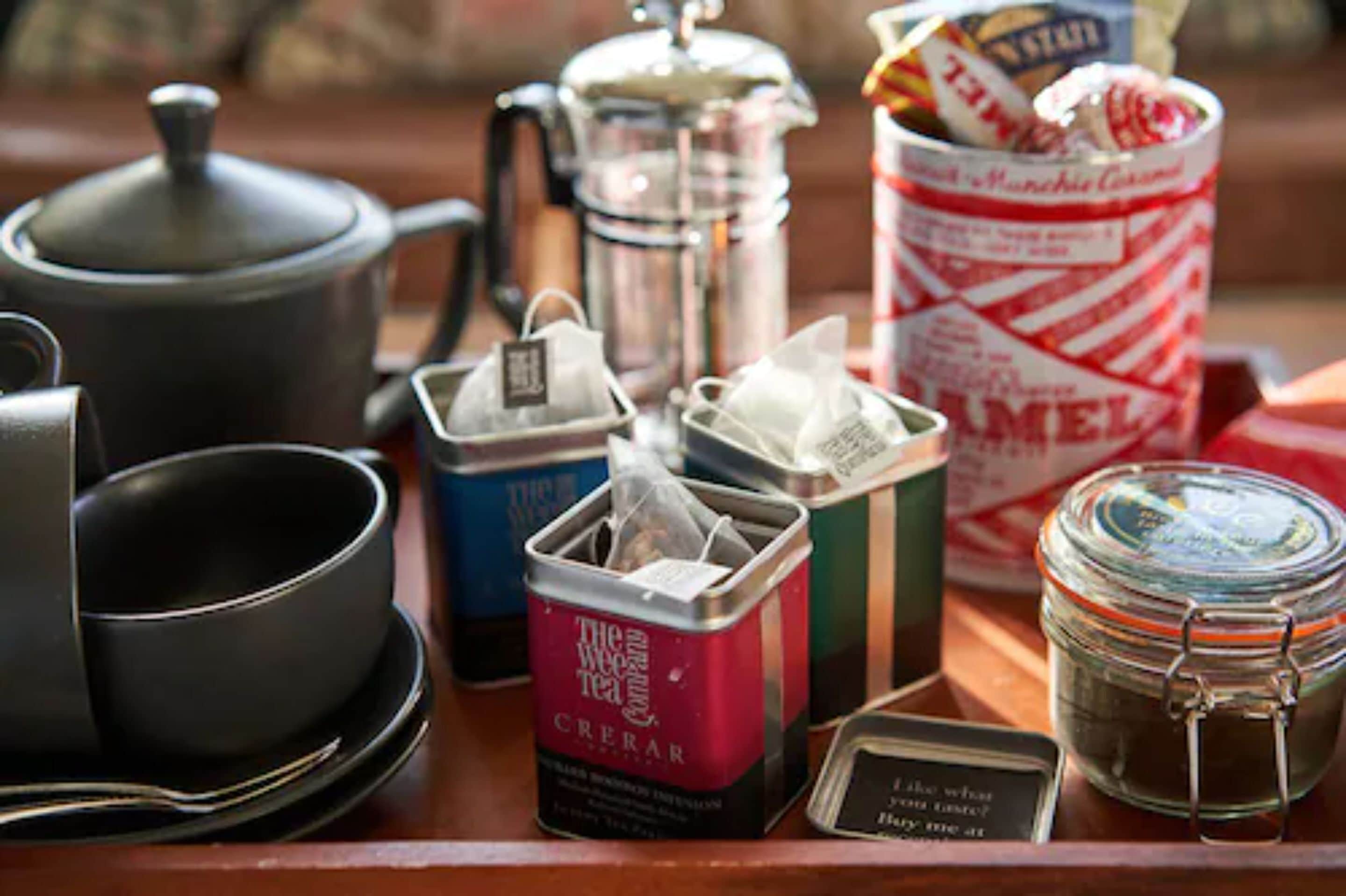 A table with a coffee maker, tea bags, a jar of sugar, and a sign with a message.
