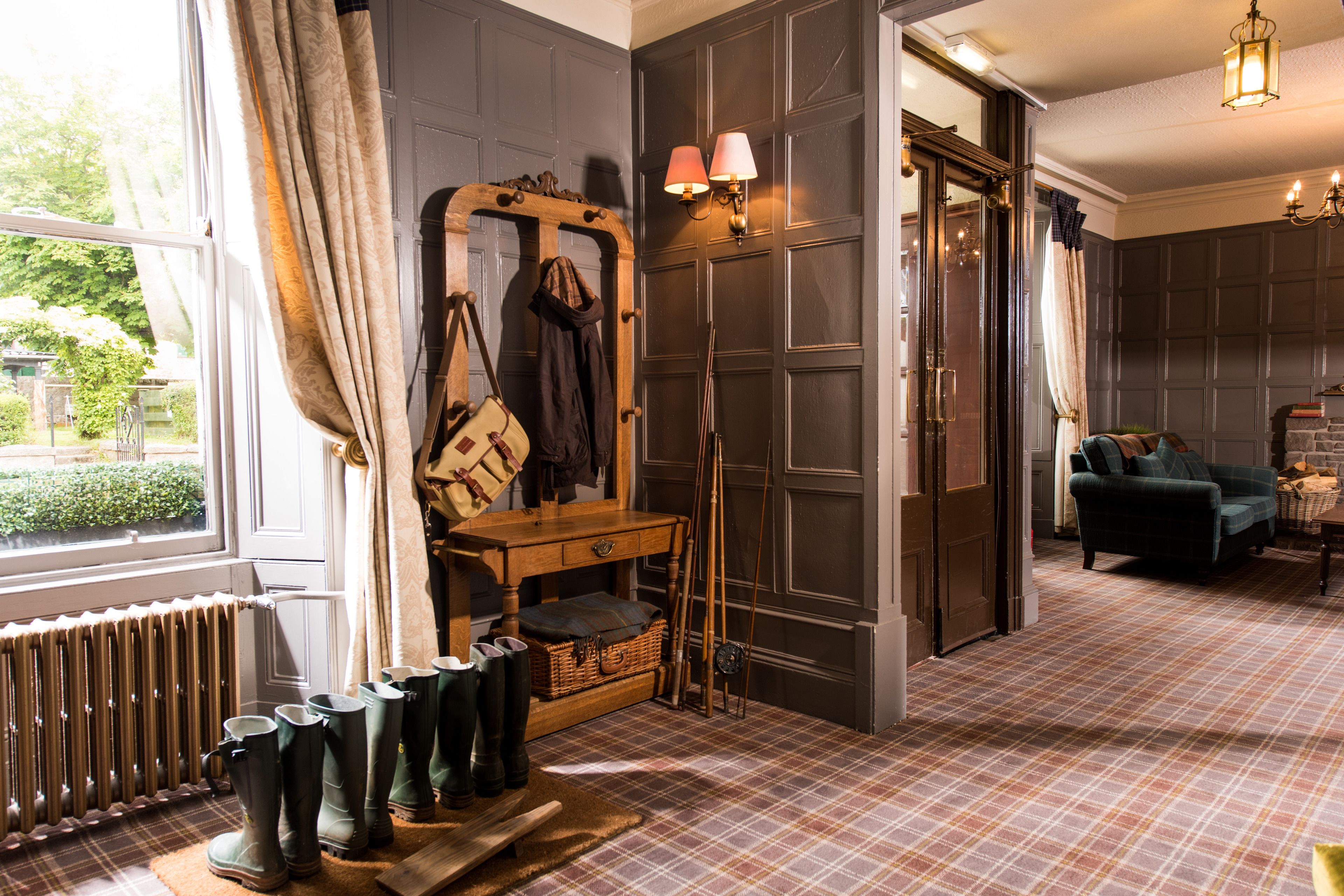 A room with a plaid carpet, a wooden bench with boots, a mirror, and a green armchair.