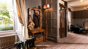 A room with a plaid carpet, a wooden bench with boots, a mirror, and a green armchair.