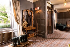 A room with a plaid carpet, a wooden bench with boots, a mirror, and a green armchair.