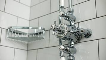 A bathroom with a chrome shower control panel, a glass shower tray, and white tiled walls.