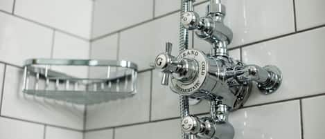 Un baño con panel de control de ducha cromado, plato de ducha de vidrio y paredes cubiertas de azulejos blancos.