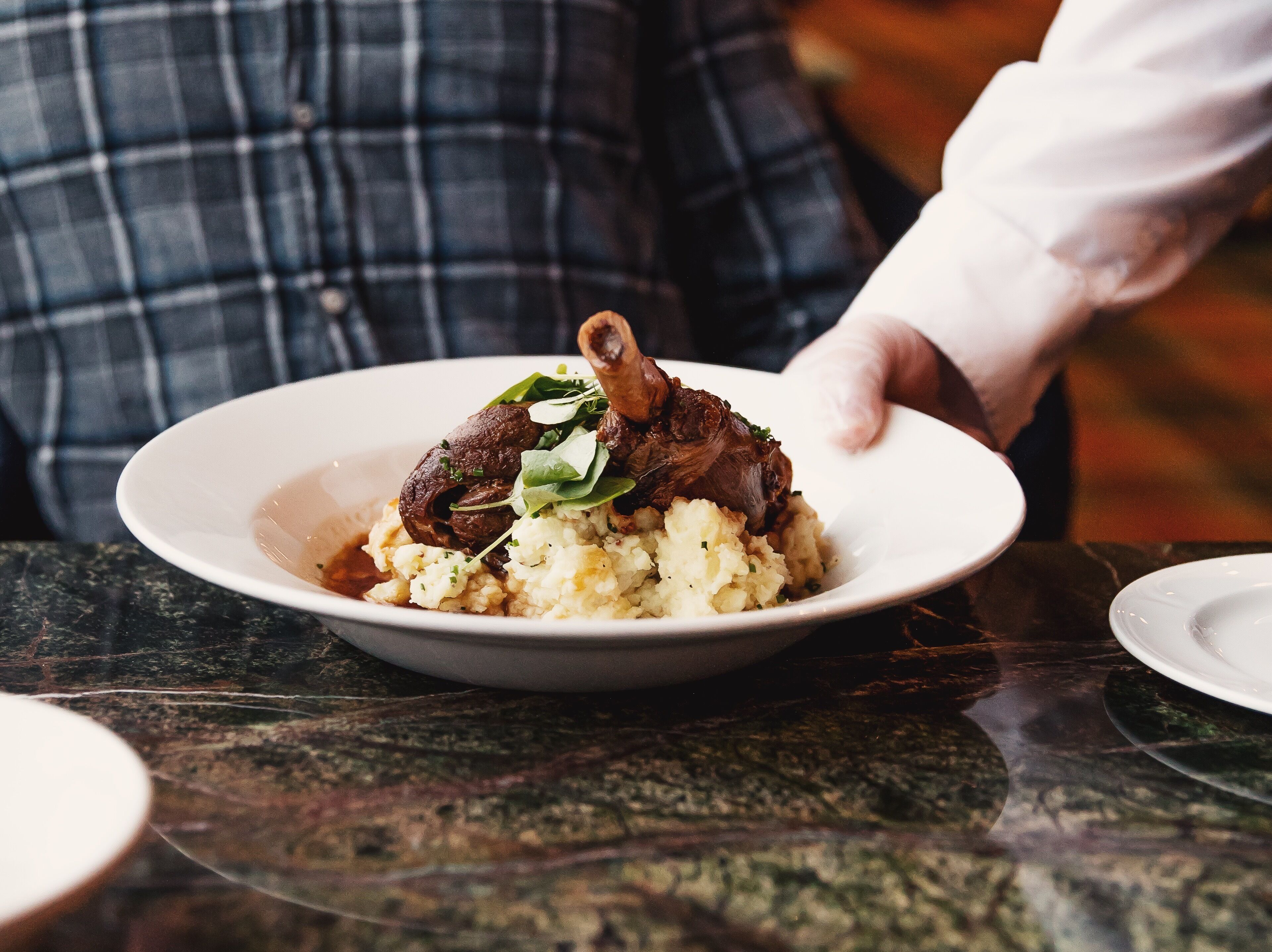 A plate of food with mashed potatoes and a piece of meat, possibly lamb, garnished with greens.
