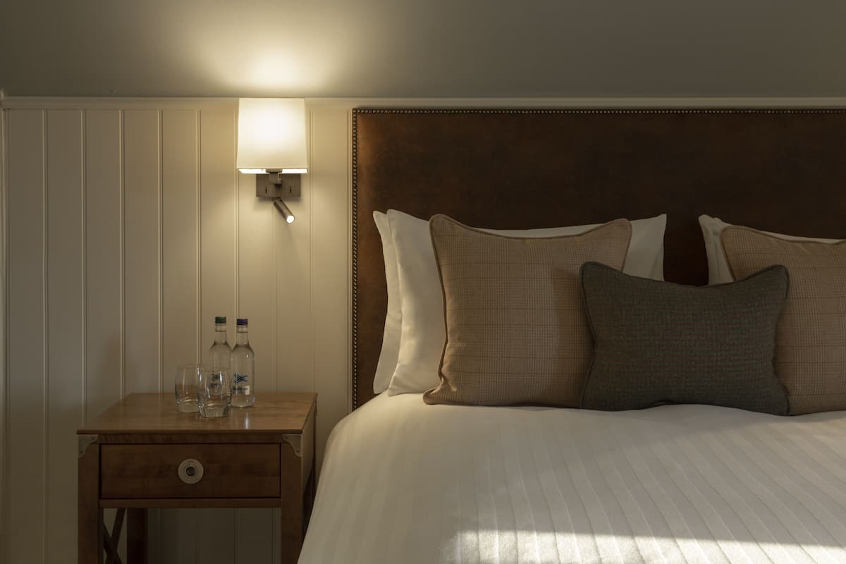 A neatly made bed with a wooden headboard, a bedside table with a lamp, and a small drawer.