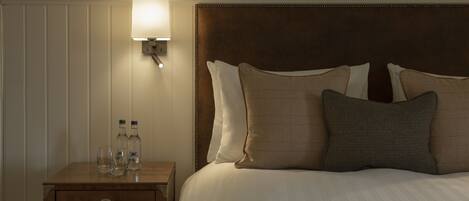 A neatly made bed with a wooden headboard, a bedside table with a lamp, and a small drawer.
