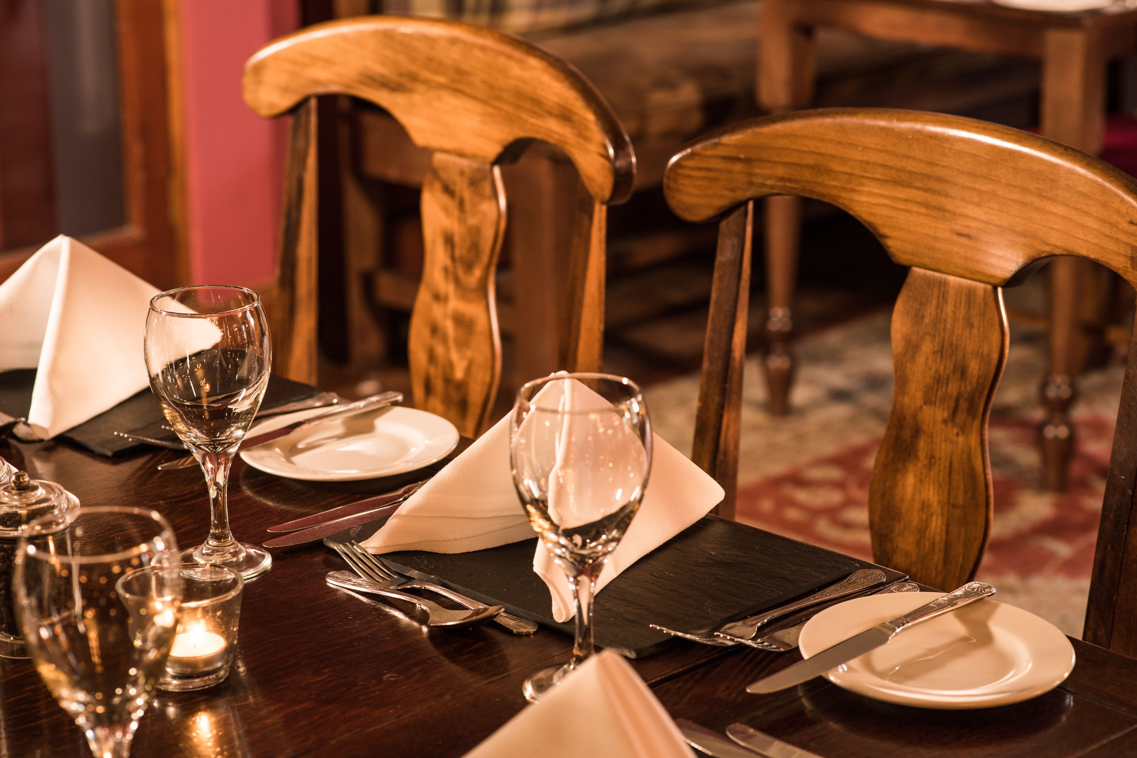 A dining table set with a wine glass, a candle, and cutlery.
