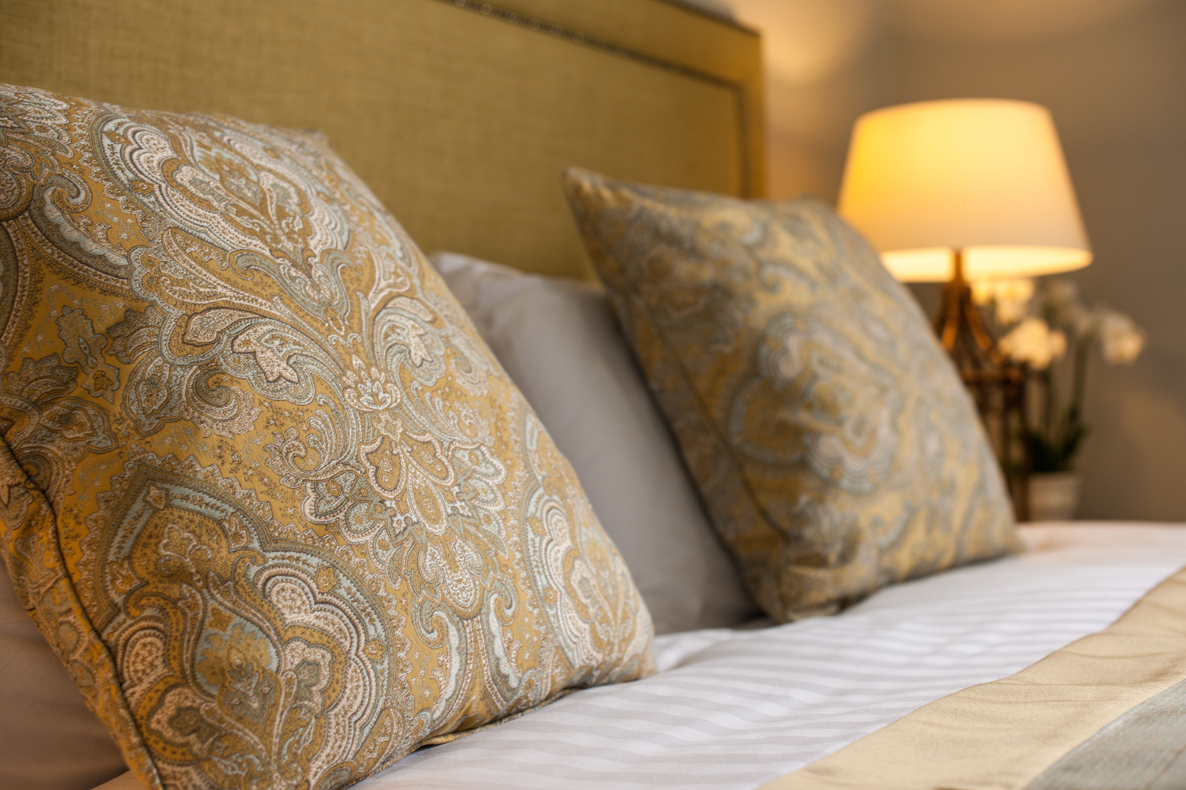 A bed with patterned pillows and a lamp in the background.
