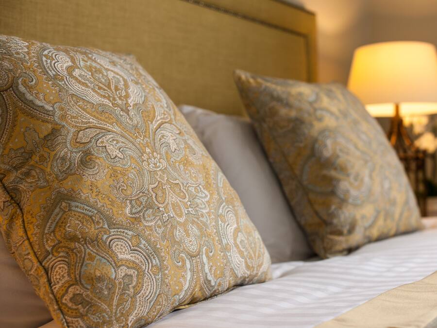 A bed with patterned pillows and a lamp in the background.
