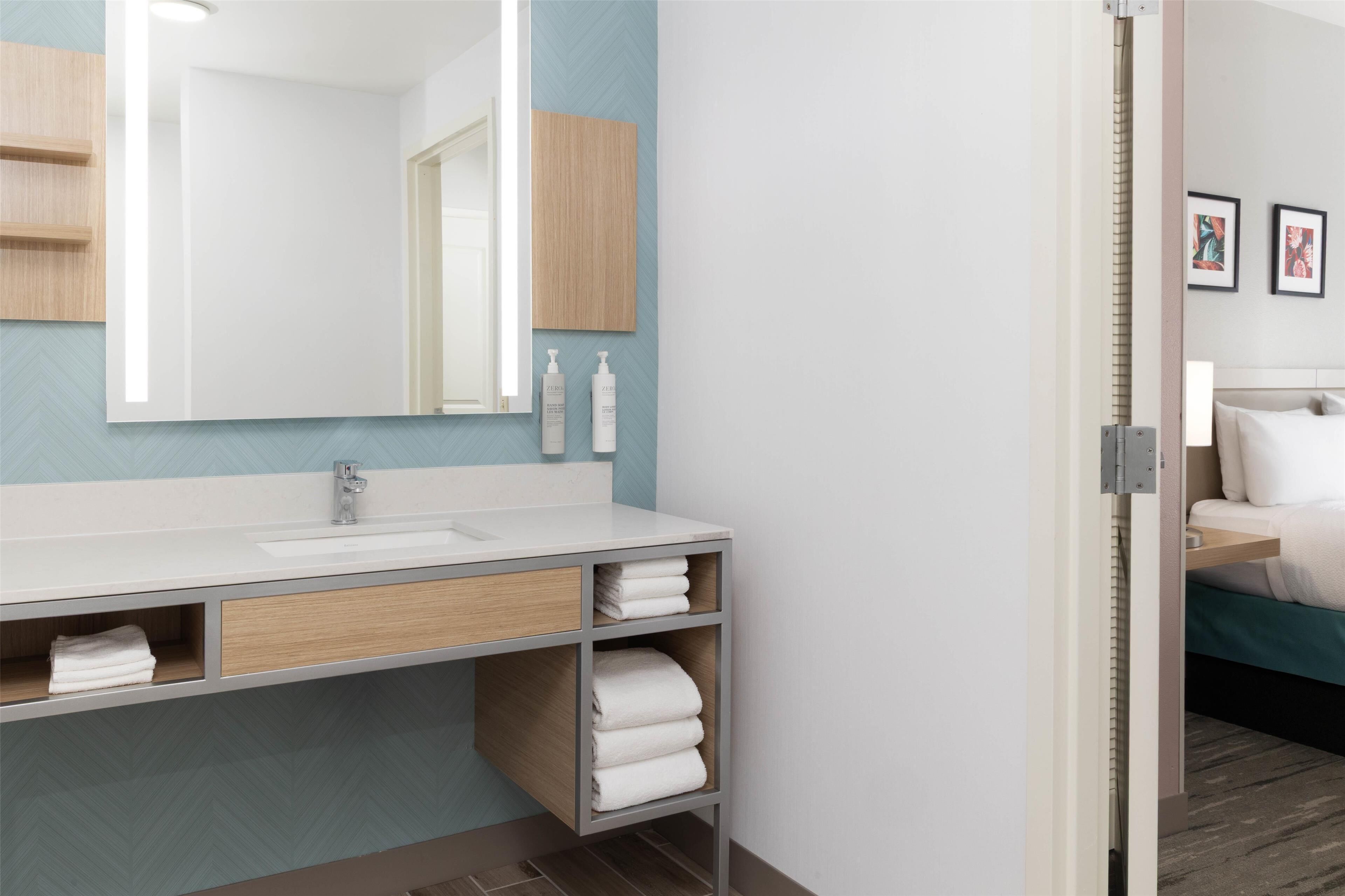 A modern bathroom with a large mirror, white sink, and wooden shelves.