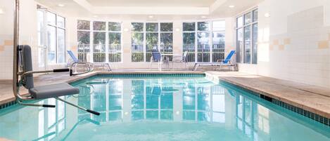 Una piscina interior con agua azul cristalina, una silla de socorrista y una escalera de piscina.