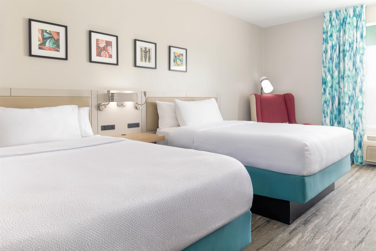 Een hotelkamer met twee bedden, een nachtkastje met een lamp en een wanddecoratie.