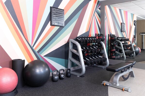 Un gimnasio con equipo de ejercicio, una pared con rayas de colores y un banco.