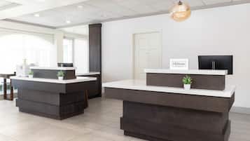 A modern hotel reception area with two reception desks, a large window, and a sign indicating 'Hilton Honors'.