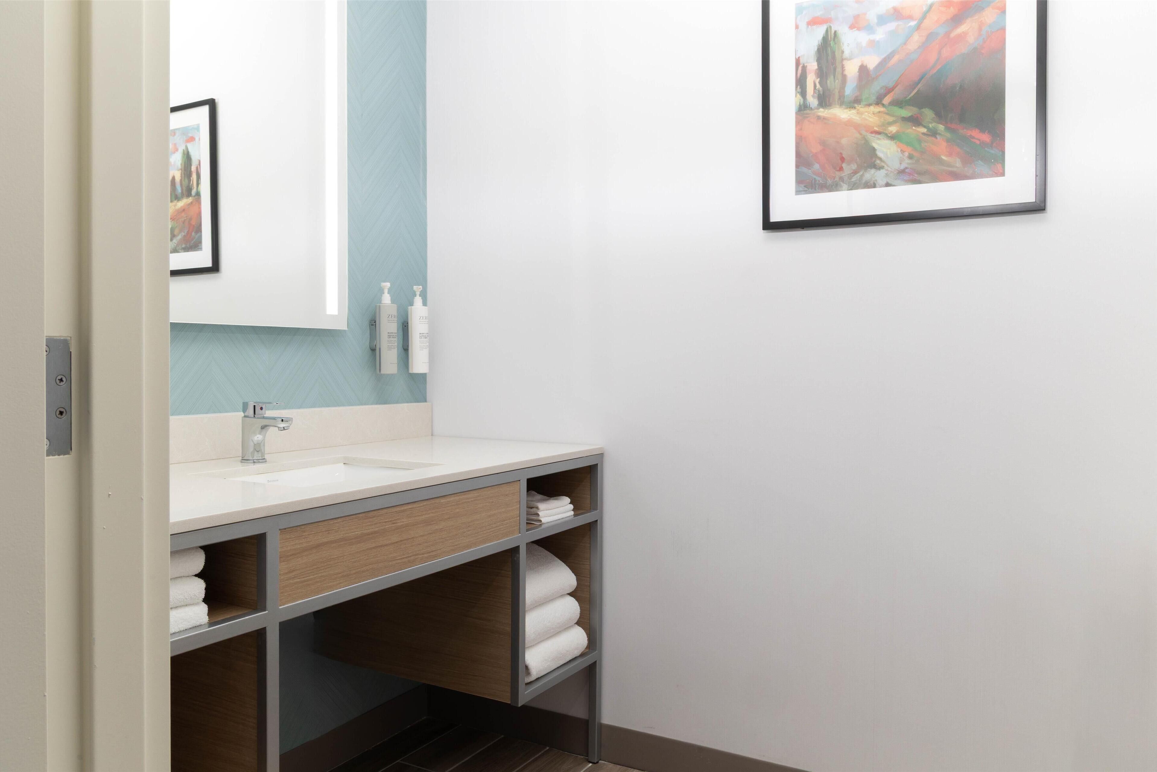 Un baño moderno con un lavamanos blanco, tocador de madera y un cuadro en la pared.