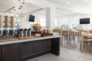 A modern breakfast area with a self-serve station, seating, and large windows. - Hilton Garden Inn Ontario/Rancho Cucamonga (Rancho Cucamonga)